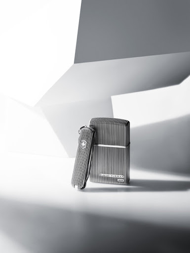 Still life studio shot of a metal Swiss Army knife and a lighter with vertical striped patterns against a white and grey geometric background.