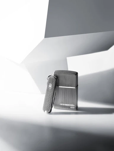 Still life studio shot of a metal Swiss Army knife and a lighter with vertical striped patterns against a white and grey geometric background.