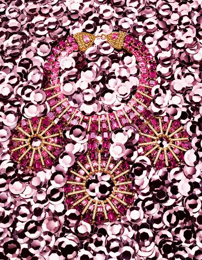 Pink and gold jeweled necklace, bracelet, and earrings displayed on a bed of shiny pink sequins, shot with an eye-level, medium framing.
