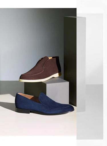 Studio shot showcasing a brown leather boot and a navy blue suede loafer, elegantly arranged on geometric white and grey platforms.