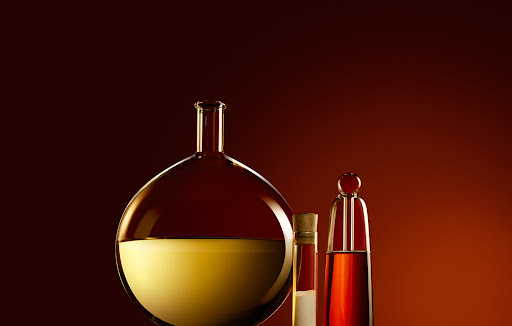 Three glass bottles with amber liquids sit against a warm background gradient, creating a simple and elegant chemical composition.
