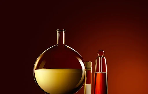 Three glass bottles with amber liquids sit against a warm background gradient, creating a simple and elegant chemical composition.