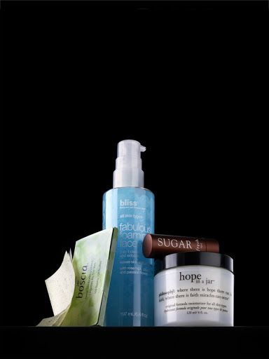 Still life shot of Bliss foaming face wash, Sugar lip treatment, Boscia cleansing cloths, and Hope in a Jar moisturizer on black.