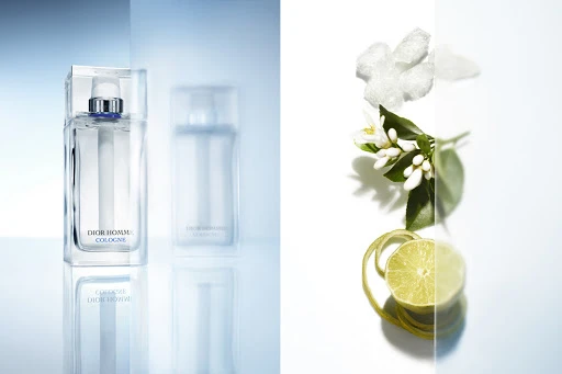 Dior Homme Cologne fragrance with citrus fruit and flowers on a white background, showcasing its fresh and aromatic composition.