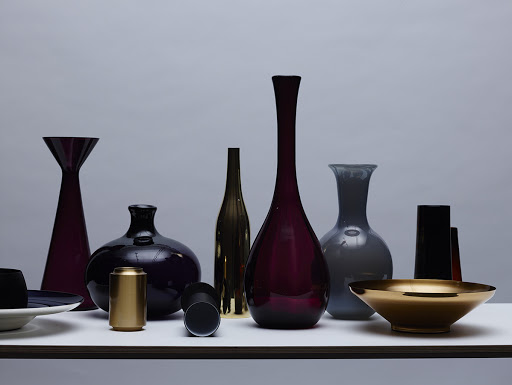 Still life featuring an array of glassware vases and metallic decorative bowls, arranged on a white surface against a neutral backdrop.