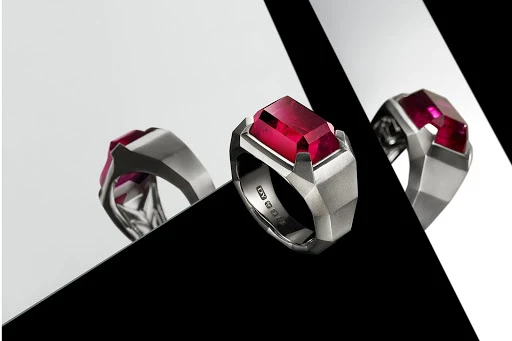Three jewelry rings featuring a silver band and a rectangular ruby stone, arranged against a contrasting black and white background.