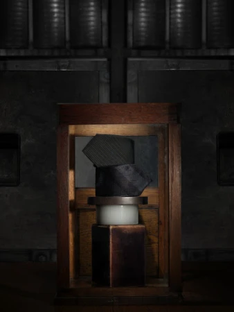 Still life shot of stacked ties in a wooden frame atop white and dark brown pedestals, set against a dark, industrial background.