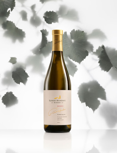 Elegant bottle of Robert Mondavi Reserve white wine on a white surface with soft shadows and leaf pattern in the background.
