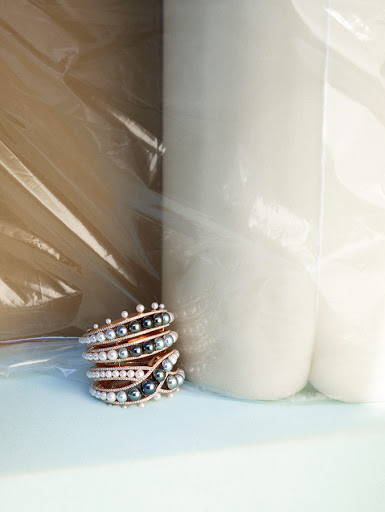 Stack of pearl bracelets on a light blue surface, with white cylindrical objects behind, enclosed in transparent packaging.