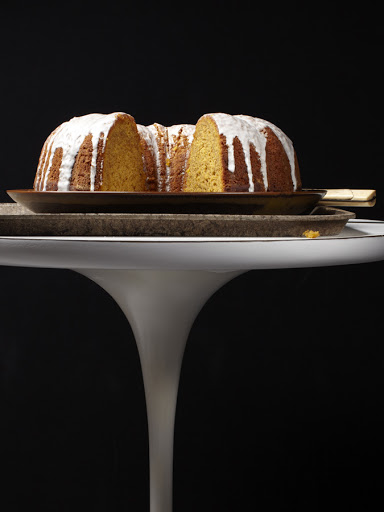 Overhead shot of a sliced Bundt cake with icing on a brown plate, displayed on a white tulip table against a dark background.