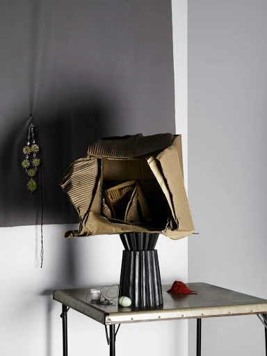 Unique table lamp with cardboard shade on metal table against gray wall, modern interior design, creative lighting fixture.