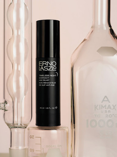 Erno Laszlo skincare product, Timeless Night Age Relief, in black pump bottle on lab glassware, soft pink backdrop, beauty product.