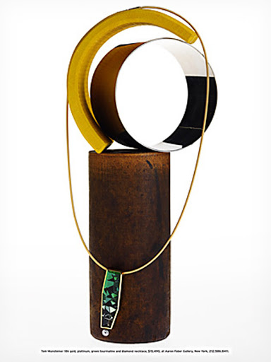 An abstract still life sculpture featuring a green gemstone necklace draped over a vertical cylindrical base against white