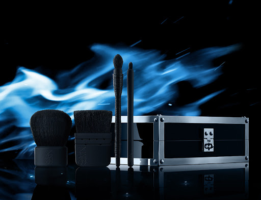 Cosmetic product arrangement with makeup brushes and case against a black backdrop with blue light effects, beauty product photography.