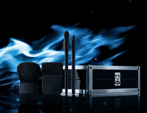 Cosmetic product arrangement with makeup brushes and case against a black backdrop with blue light effects, beauty product photography.