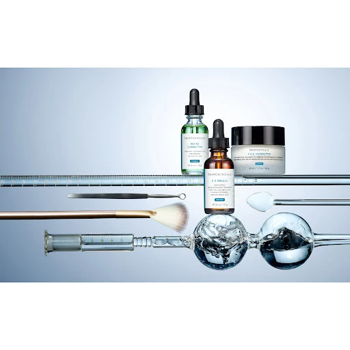 Cosmetic products including bottles and a jar are displayed with applicators on a reflective surface against a light blue background.