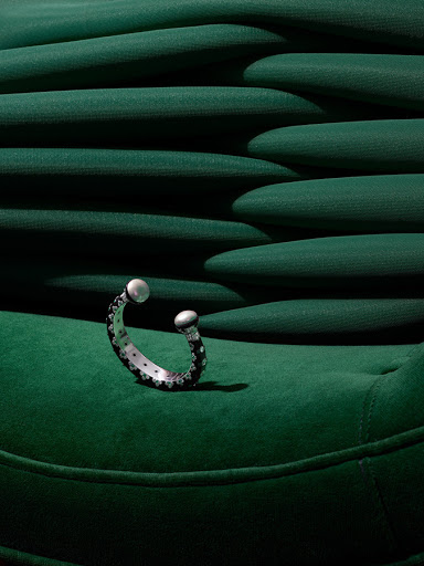 Close-up studio shot of a black and silver cuff bracelet with pearl-like ends on a green, textured surface, highlighting jewelry design.