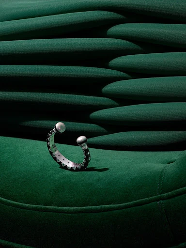 Close-up studio shot of a black and silver cuff bracelet with pearl-like ends on a green, textured surface, highlighting jewelry design.