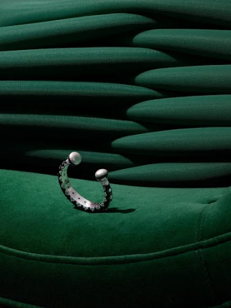 Close-up studio shot of a black and silver cuff bracelet with pearl-like ends on a green, textured surface, highlighting jewelry design.
