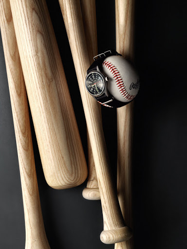 Baseball with a wristwatch resting on it, propped up by wooden baseball bats against a dark background, product photography.