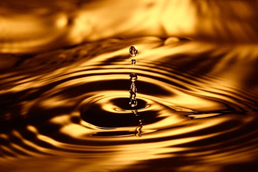 Close-up of water droplet collision creating ripples on a golden fluid surface with a shallow depth of field and warm lighting.
