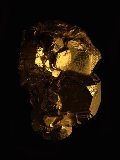 Close-up studio shot of a gold-colored pyrite mineral formation against a stark black background. The pyrite displays geometric shapes.