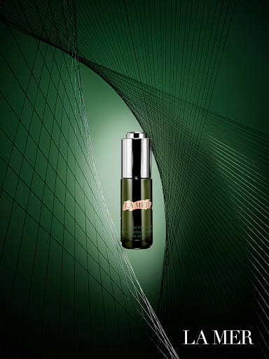 La Mer Renewal Oil bottle on a green background with abstract line art, advertising product photography in a beauty and fashion context.