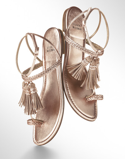 Stuart Weitzman gold-tone sandals with braided straps and tassels, photographed on a white background. Fashionable women's footwear.