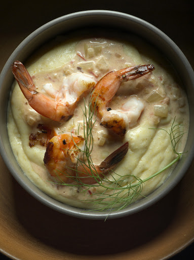Overhead shot of a bowl of shrimp and grits with garnish, showcasing the creamy texture and vibrant colors of the dish in a close-up view.