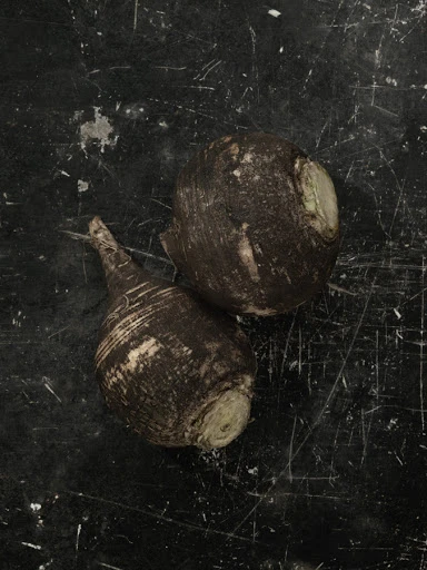 Two black radishes are placed on a black surface with scratches, creating a simple and textured still life image.