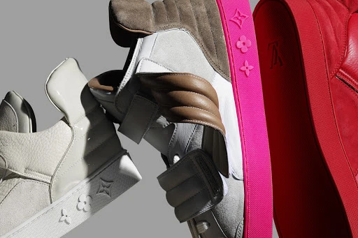 A close-up studio shot showcases three luxury sneakers, each featuring distinct colors and textures, arranged against a neutral gray backdrop.