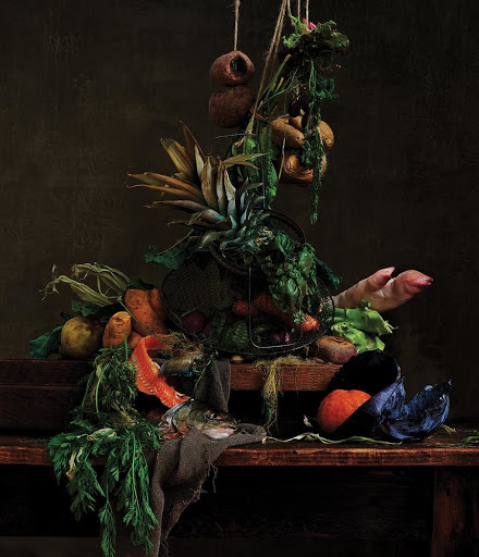 Still life arrangement with vegetables, pineapple, fish, and meat on a wooden table against a dark brown background, captured in studio photography.