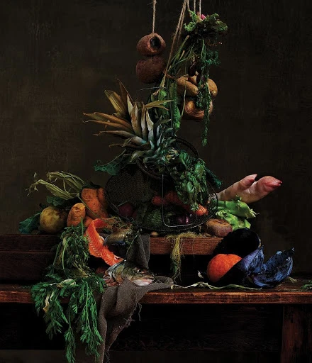 Still life arrangement with vegetables, pineapple, fish, and meat on a wooden table against a dark brown background, captured in studio photography.