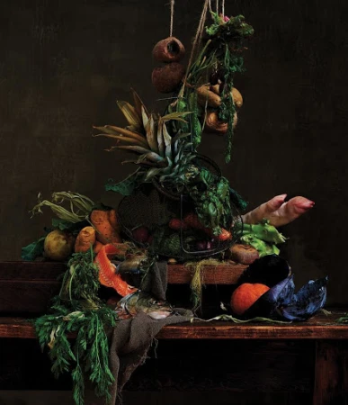 Still life arrangement with vegetables, pineapple, fish, and meat on a wooden table against a dark brown background, captured in studio photography.