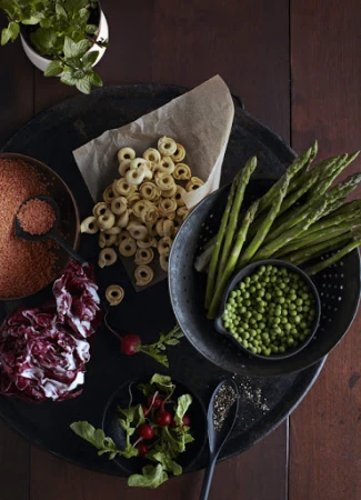 Overhead shot of uncooked pasta rings, asparagus spears, peas, radicchio, and radishes arranged on a dark wooden table.