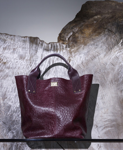 Burgundy leather tote bag with handles, featuring a textured pattern, set against a light grey textured stone slab background.