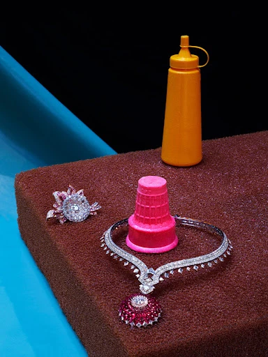 Still life of jewelry and an orange condiment bottle on a brown surface with blue and black background.