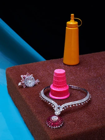Still life of jewelry and an orange condiment bottle on a brown surface with blue and black background.