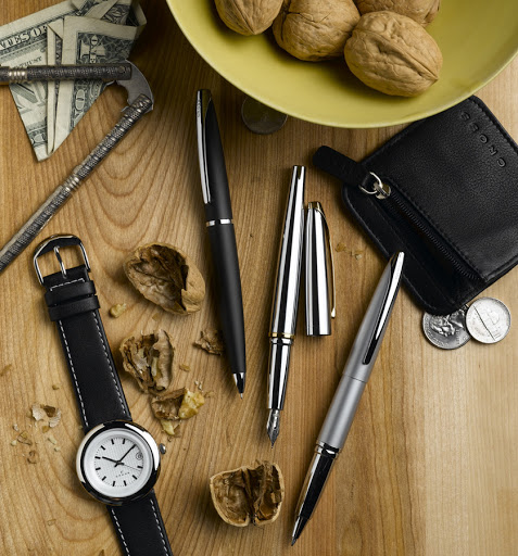 Still life shot on wood surface with pens, wristwatch, wallet, currency, walnuts, and a nutcracker arranged in an overhead composition.