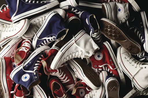 Pile of red, white, and navy blue Converse sneakers with white laces and soles, arranged in a high-angle studio shot.