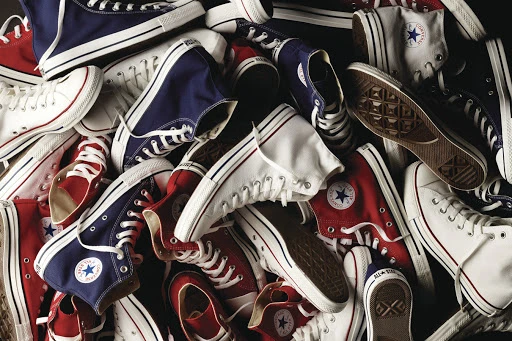 Pile of red, white, and navy blue Converse sneakers with white laces and soles, arranged in a high-angle studio shot.