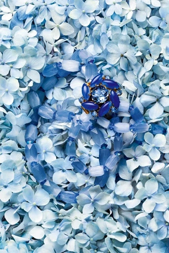 Close-up of a floral jewelry ring on a bed of blue hydrangea petals creating a natural and elegant backdrop for high-end jewellery.