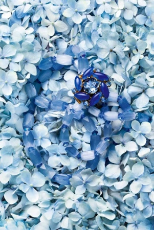 Close-up of a floral jewelry ring on a bed of blue hydrangea petals creating a natural and elegant backdrop for high-end jewellery.