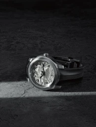 A luxury silver wristwatch with a dark textured band resting on a dark stone surface under a streak of light