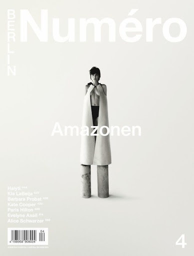Black-and-white fashion magazine cover featuring a female model in avant-garde apparel, standing on cylinders, with the magazine's title at the top.