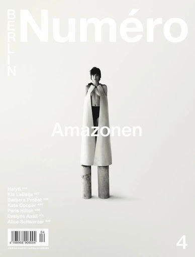 Black-and-white fashion magazine cover featuring a female model in avant-garde apparel, standing on cylinders, with the magazine's title at the top.