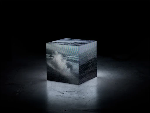 Abstract cube with ocean wave imagery on a dark marble surface, illuminated in a black studio setting, creating a surreal atmosphere.