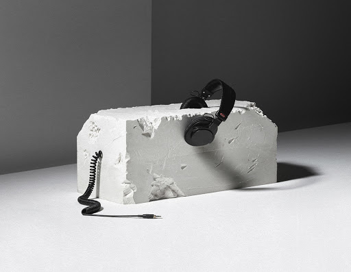 Studio shot of black over-ear headphones resting on a textured white block against a gray background with a coiled audio cable.
