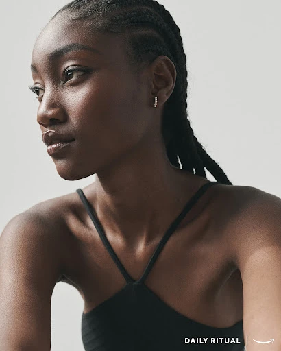 Close-up studio shot of a young Black woman with braided hair, wearing a black top and earrings, looking off to the side.