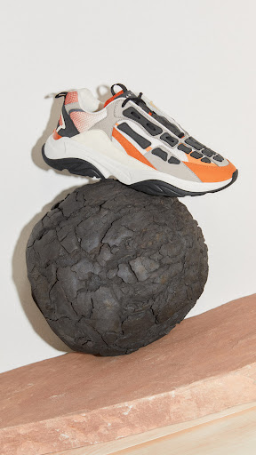 Studio shot of a fashion sneaker balanced on a dark stone sphere and a pink stand against a white backdrop.